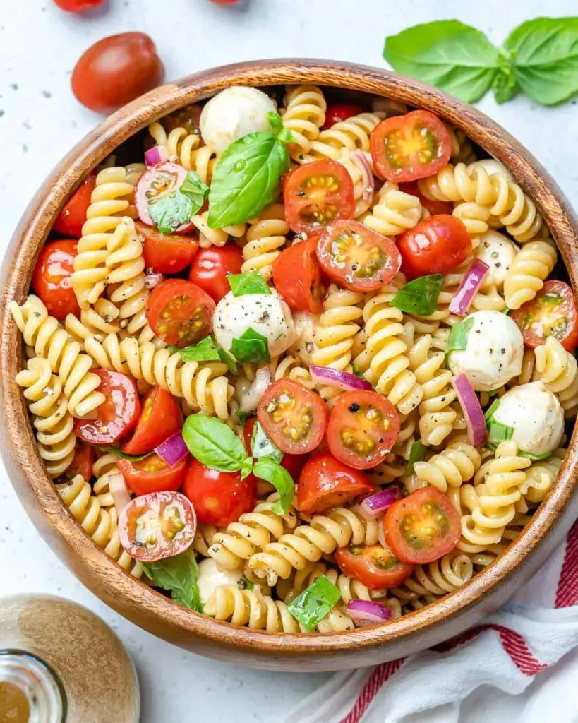 A bowl of colorful pasta salad with Caprese ingredients, including cherry tomatoes, fresh mozzarella balls, basil leaves, and cooked pasta, drizzled with balsamic glaze, a delightful summer meal.