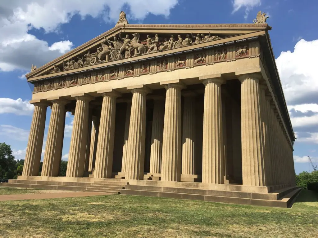 Exterior view of the Parthenon replica in Nashville's Centennial Park, surrounded by lush greenery and under a bright blue sky.