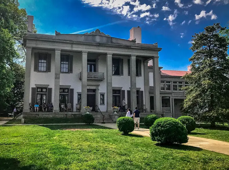 Exterior view of the Belle Meade Plantation, a historic antebellum estate in Nashville, surrounded by lush gardens and towering trees, offering visitors a glimpse into the region's rich history.