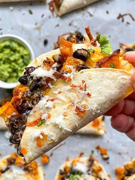 A platter of vibrant butternut squash and black bean tacos, featuring colorful roasted squash cubes, hearty black beans, crisp lettuce, diced tomatoes, and zesty salsa, all nestled in warm tortillas and garnished with fresh cilantro.