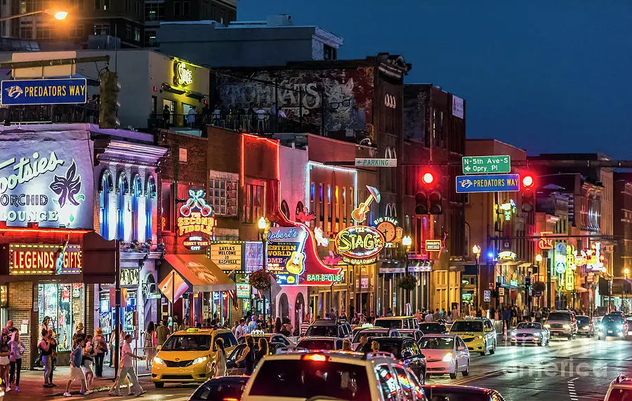 A vibrant street scene of Broadway in Nashville, Tennessee, filled with neon lights, bustling crowds, and iconic music venues, capturing the energy and excitement of the city's famous entertainment district.