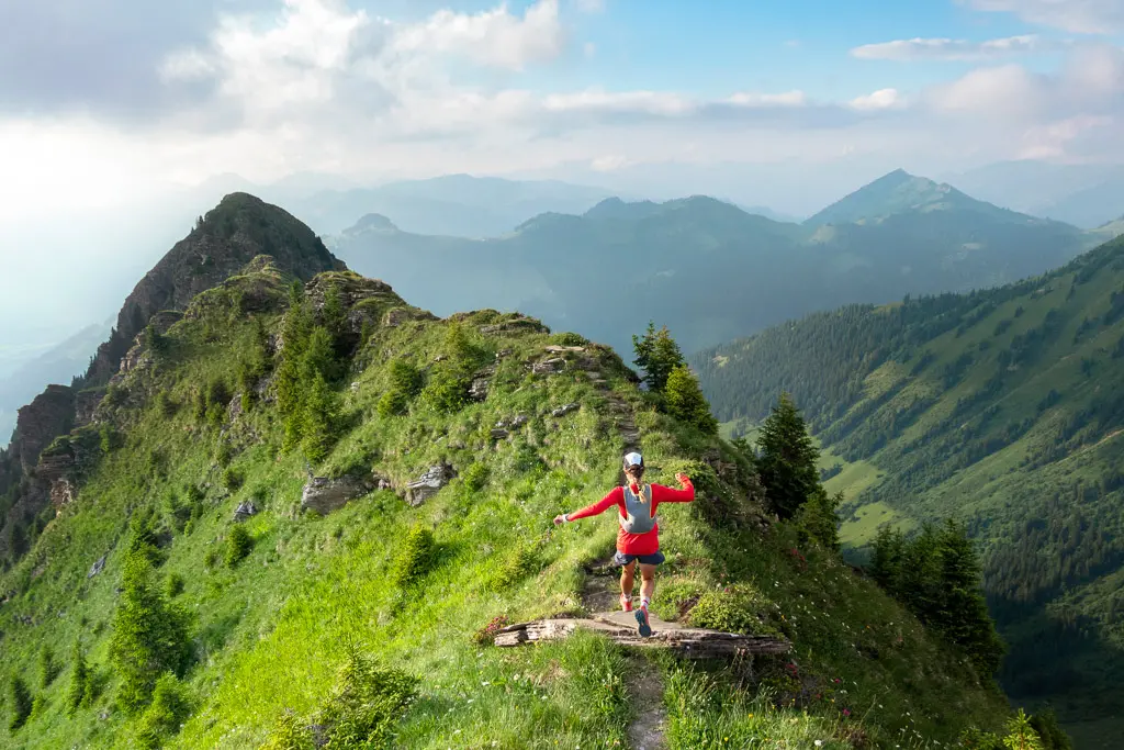 A lone girl standing on a rocky mountain peak, with majestic mountains and blue sky in the background, enjoying the scenic beauty of the wilderness.