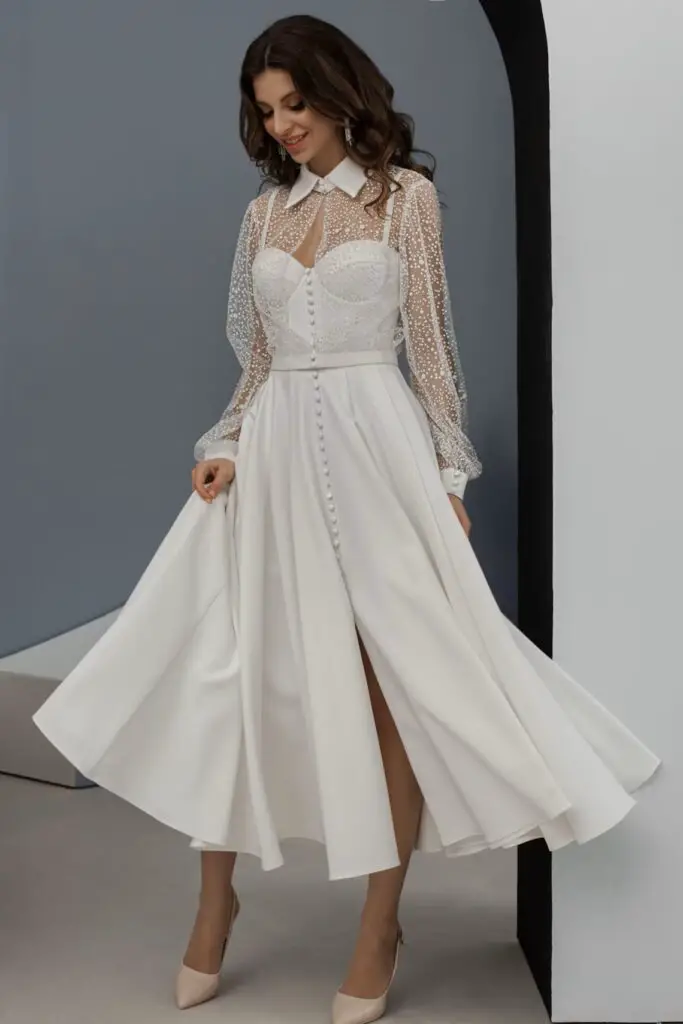 A woman standing in a white midi dress adorned with delicate pearl embellishments, exuding elegance and sophistication