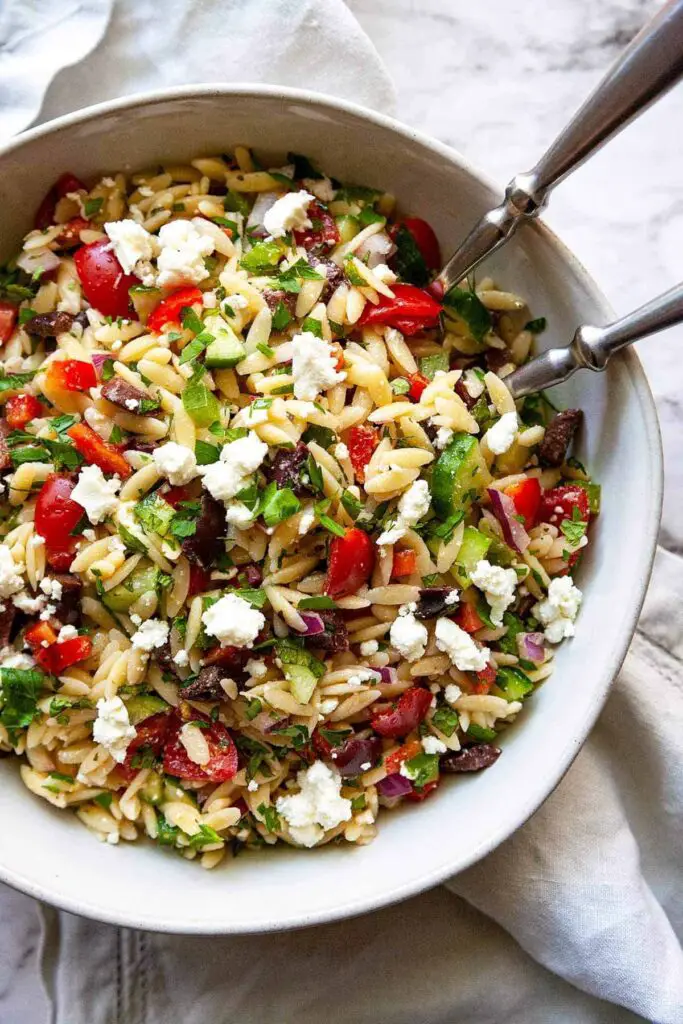 A bowl of vibrant salad with orzo pasta, featuring colorful vegetables like cherry tomatoes, cucumbers, bell peppers, and fresh herbs, tossed in a light vinaigrette dressing, a refreshing summer dish.