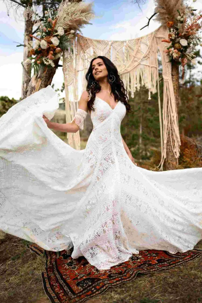 A woman stands in boho-inspired wedding dress, with a picturesque floral background enhancing the natural ambiance.