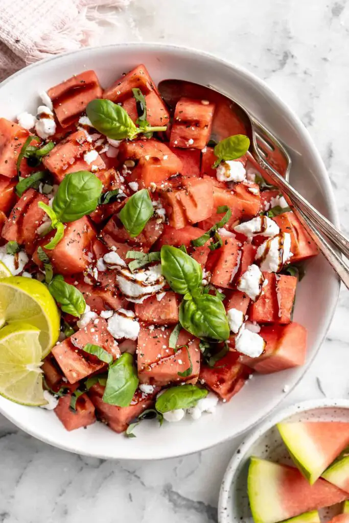 A colorful bowl filled with diced watermelon, crumbled feta cheese, and fresh mint leaves, drizzled with a tangy vinaigrette dressing.